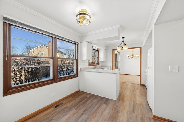 kitchen featuring decorative light fixtures, white cabinetry, sink, ornamental molding, and light wood-type flooring