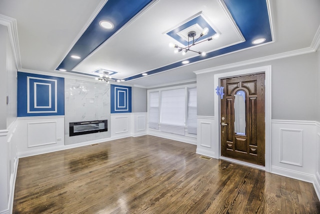 unfurnished living room with a fireplace, ceiling fan, a tray ceiling, crown molding, and dark wood-type flooring