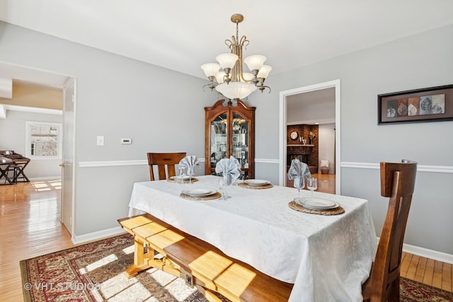 dining room featuring baseboards, light wood finished floors, a fireplace, and an inviting chandelier