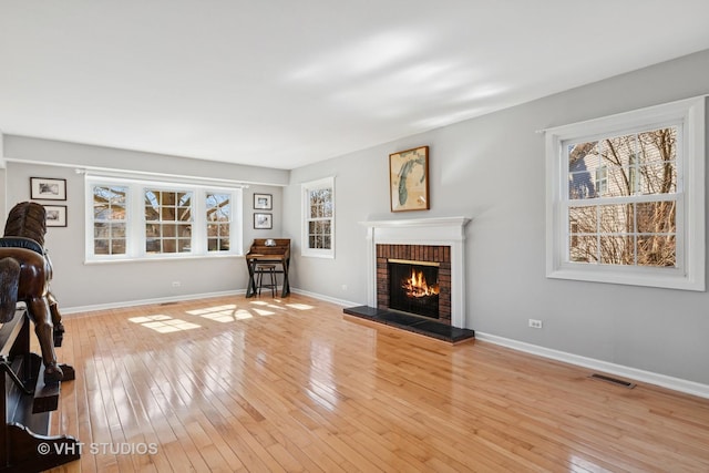 living room with a brick fireplace, wood-type flooring, visible vents, and baseboards