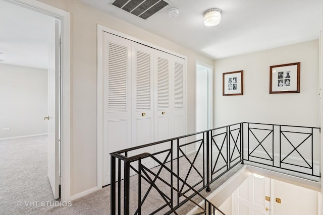 hallway with an upstairs landing, carpet, visible vents, and baseboards