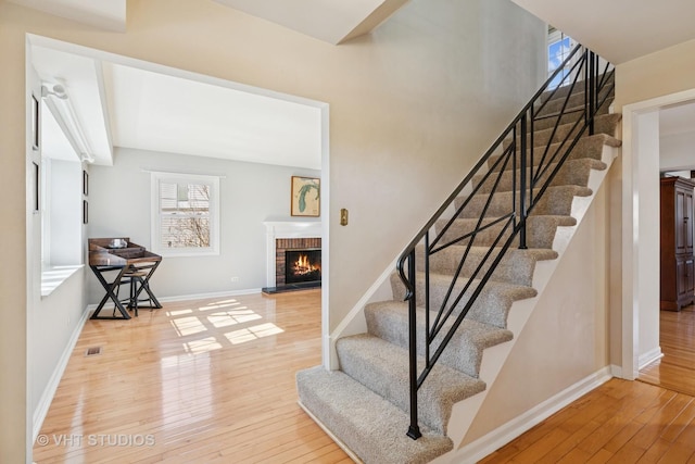 stairs featuring a brick fireplace, wood-type flooring, visible vents, and baseboards