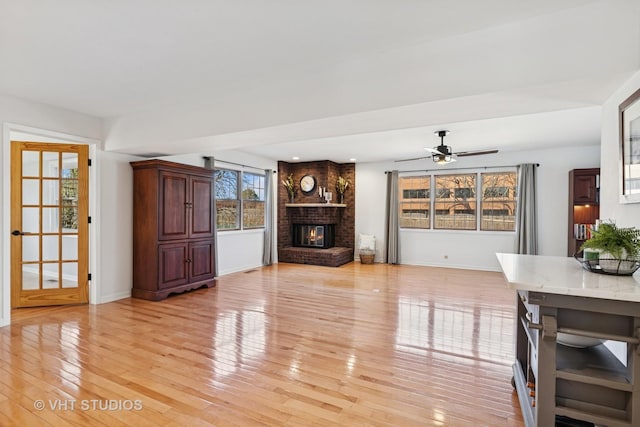 unfurnished living room with a ceiling fan, a fireplace, light wood-style flooring, and baseboards