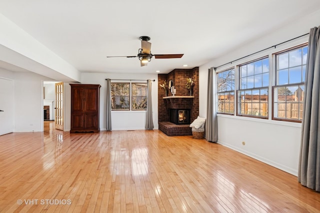 unfurnished living room featuring a brick fireplace, baseboards, light wood finished floors, and a ceiling fan