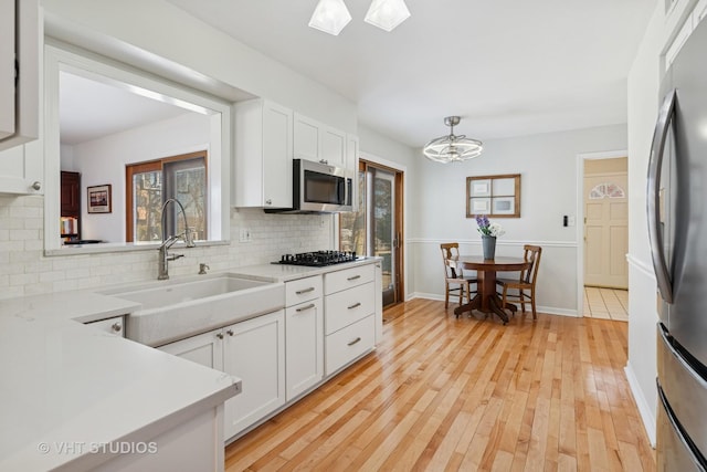 kitchen featuring light wood-style flooring, a sink, white cabinetry, light countertops, and appliances with stainless steel finishes