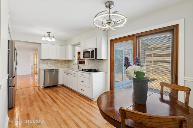 kitchen with appliances with stainless steel finishes, a chandelier, white cabinets, and a sink