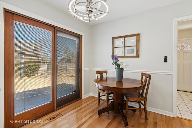 dining space featuring light wood-type flooring, visible vents, a notable chandelier, and baseboards