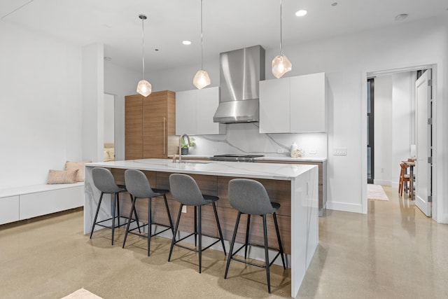 kitchen with white cabinetry, wall chimney exhaust hood, a kitchen island with sink, and hanging light fixtures