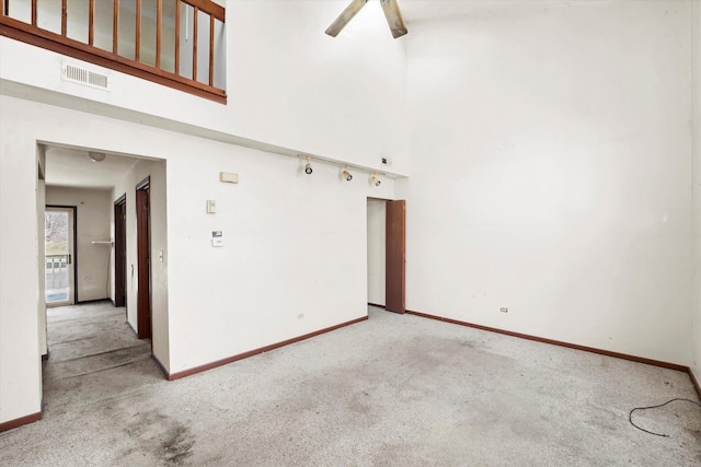 carpeted empty room with a towering ceiling and ceiling fan