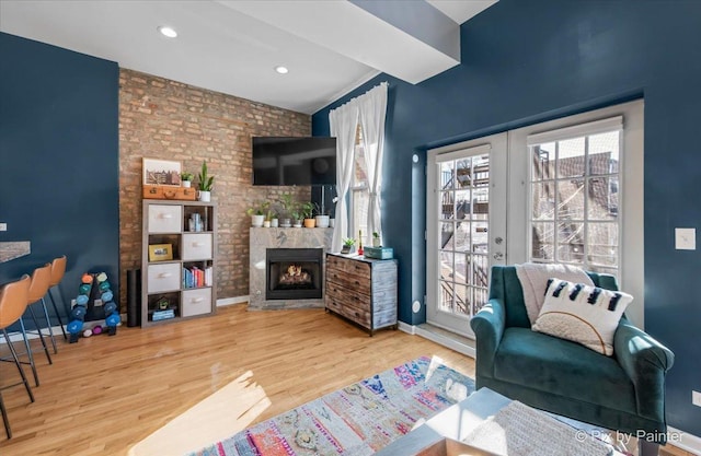 living room with brick wall, a brick fireplace, light hardwood / wood-style floors, and french doors