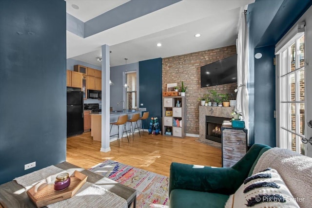 living room with brick wall, sink, a fireplace, and light wood-type flooring