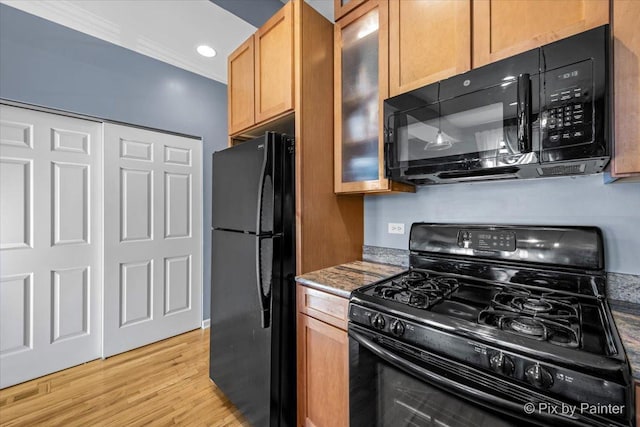 kitchen featuring ornamental molding, light hardwood / wood-style flooring, dark stone counters, and black appliances