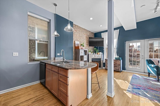 kitchen with decorative light fixtures, dishwasher, sink, dark stone counters, and light wood-type flooring