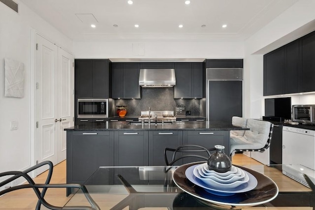 kitchen with ventilation hood, built in microwave, sink, and dark stone counters