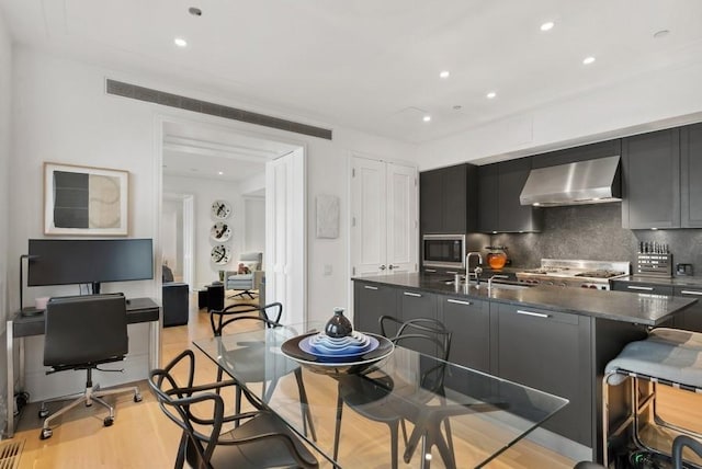 kitchen featuring wall chimney range hood, sink, light hardwood / wood-style flooring, backsplash, and stainless steel microwave