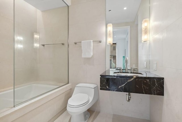 full bathroom with tile walls, sink, bath / shower combo with glass door, and toilet