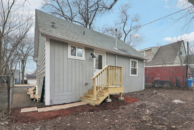 back of house with a shingled roof and fence