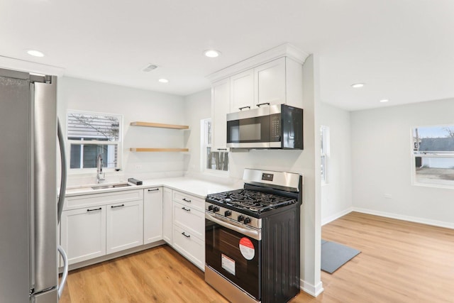 kitchen with appliances with stainless steel finishes, a wealth of natural light, a sink, and light wood-style flooring