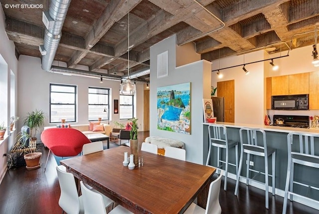 dining space featuring dark wood-type flooring, a towering ceiling, and rail lighting