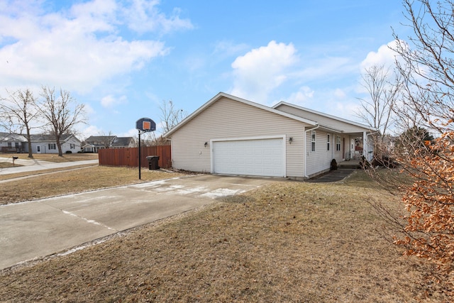 view of side of property featuring concrete driveway, a lawn, an attached garage, and fence