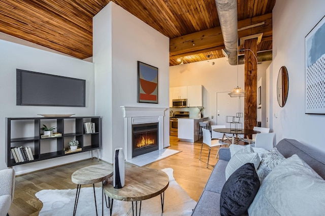 living room with beam ceiling, a high ceiling, light wood-type flooring, and wood ceiling