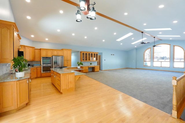 kitchen with a skylight, a large island, light stone counters, open floor plan, and stainless steel appliances