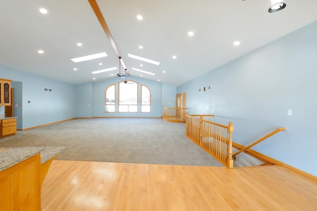 unfurnished living room with lofted ceiling with skylight, visible vents, light wood-style flooring, and baseboards