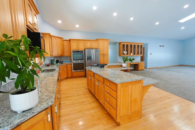 kitchen with light stone countertops, recessed lighting, a sink, appliances with stainless steel finishes, and a center island