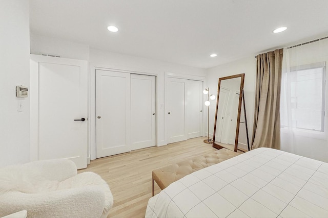 bedroom with light hardwood / wood-style flooring and multiple closets