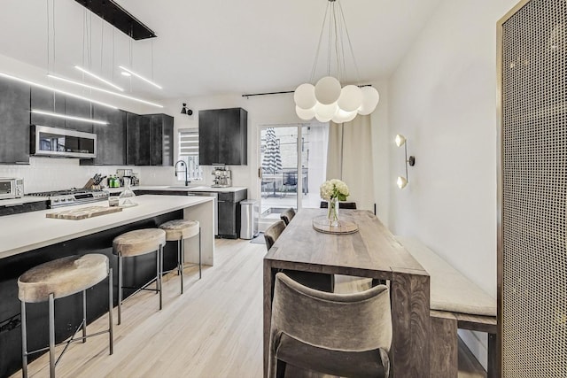 kitchen with pendant lighting, sink, a kitchen bar, decorative backsplash, and light hardwood / wood-style flooring