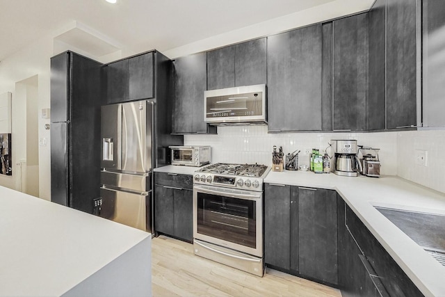 kitchen featuring appliances with stainless steel finishes, decorative backsplash, and light wood-type flooring