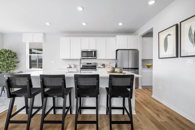 kitchen featuring light wood finished floors, stainless steel appliances, a kitchen island with sink, baseboards, and light countertops