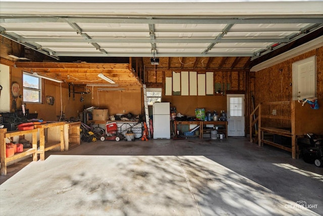 garage featuring white refrigerator, a garage door opener, and a workshop area