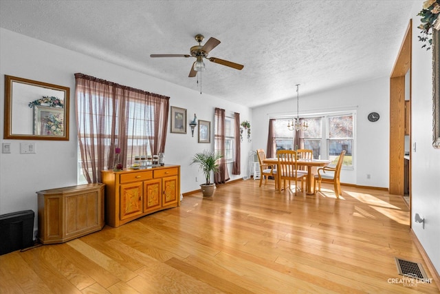 dining room featuring vaulted ceiling, ceiling fan with notable chandelier, a textured ceiling, and light wood-type flooring