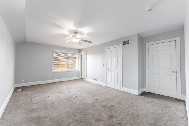 unfurnished bedroom with ceiling fan, light colored carpet, lofted ceiling, and two closets