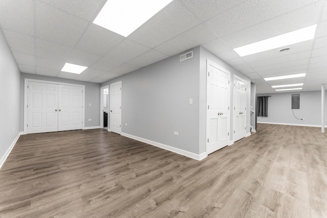 basement featuring a paneled ceiling, electric panel, and light hardwood / wood-style floors