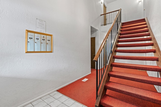 staircase with tile patterned flooring, a towering ceiling, and a mail area