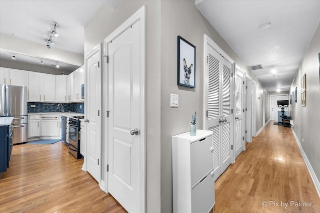 hallway featuring light wood finished floors, baseboards, visible vents, and rail lighting