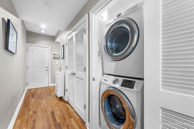 laundry area with stacked washer and dryer, light wood finished floors, laundry area, and baseboards