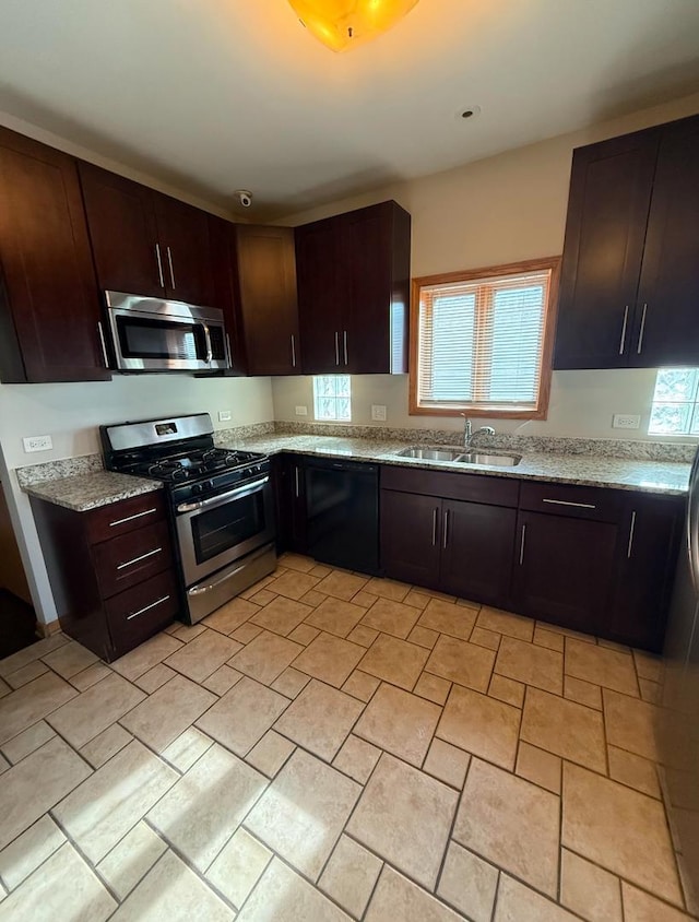 kitchen with light stone countertops, appliances with stainless steel finishes, sink, and dark brown cabinetry