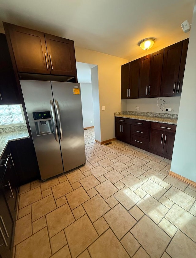 kitchen featuring dark brown cabinets, stainless steel fridge, and light stone countertops