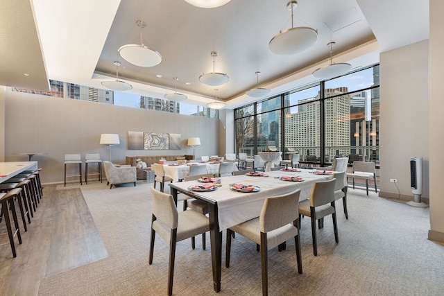 dining space featuring a city view, a raised ceiling, a high ceiling, light wood-type flooring, and baseboards