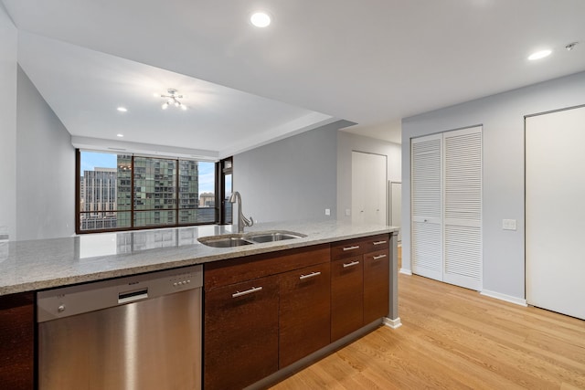 kitchen featuring light wood finished floors, light stone counters, dark brown cabinets, stainless steel dishwasher, and a sink