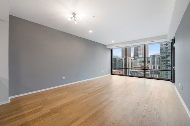 spare room featuring a view of city, expansive windows, light wood-type flooring, and baseboards