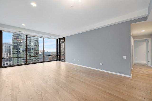 unfurnished room featuring light wood-type flooring, a city view, and baseboards