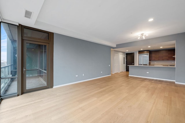 unfurnished living room featuring baseboards, a sink, visible vents, and light wood-style floors