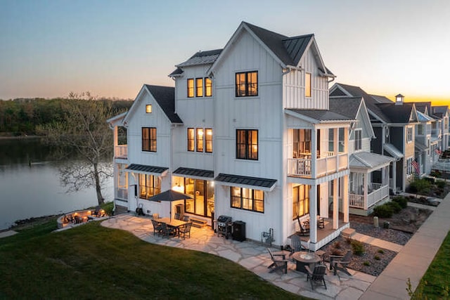 back house at dusk featuring a balcony, a lawn, and a patio area