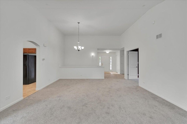 carpeted empty room featuring a notable chandelier and a high ceiling