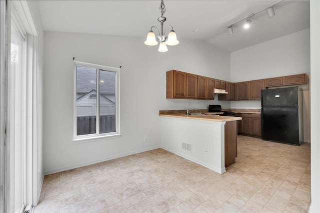 kitchen with pendant lighting, lofted ceiling, range, black fridge, and kitchen peninsula