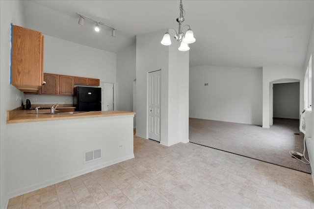 kitchen with black refrigerator, pendant lighting, sink, kitchen peninsula, and light carpet